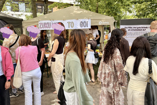 Auf dem Bild sind Besucher*innen des Sommerfests vor dem Stand "Zukunft to go"