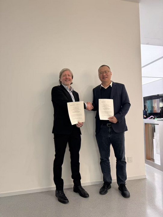 Auf dem Bild sind Prof. Dr. Chris Neuhäuser, Professor für Praktische Philosophie am Institut für Philosophie und Politikwissenschaften der Fakultät Humanwissenschaften und Theologie und Prof. Dr. Wang Jun, der Leiter der School of Philosophy, zu sehen. Beide halten das Memorandum in der einen Hand und reichen sich die andere Hand. Beide lächeln.