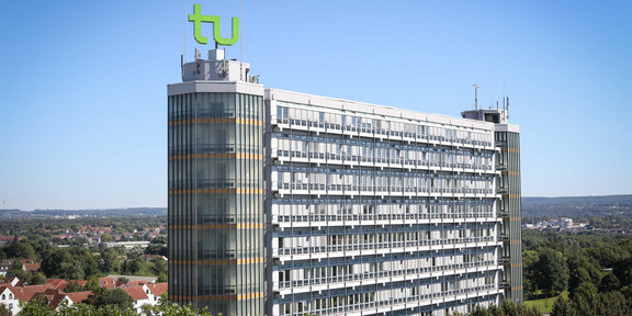 Mathematikgebäude mit Mathetower Mathematikgebäude mit Mathetower: Ein hohes Gebäude mit vielen Fenstern und je einem Turm an beiden Seiten. Auf dem linken Turm ein grünes TU-Logo. Im Hintergrund Häuser und Bäume.